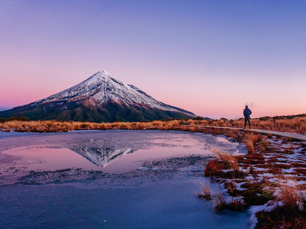 Snow-dusted Mount Taranaki reflecting in a still pool at dawn, showing the sacred mountain granted legal rights in New Zealand.